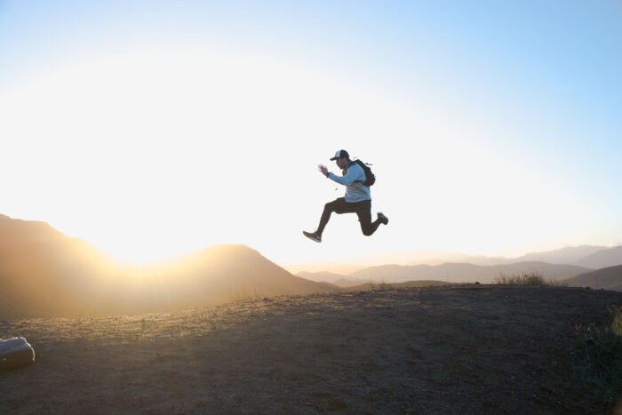 Man som hoppar på en kulle i solnedgången