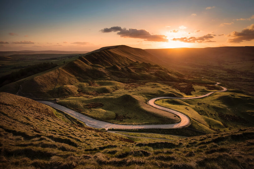 Curved road through green hills at sunset